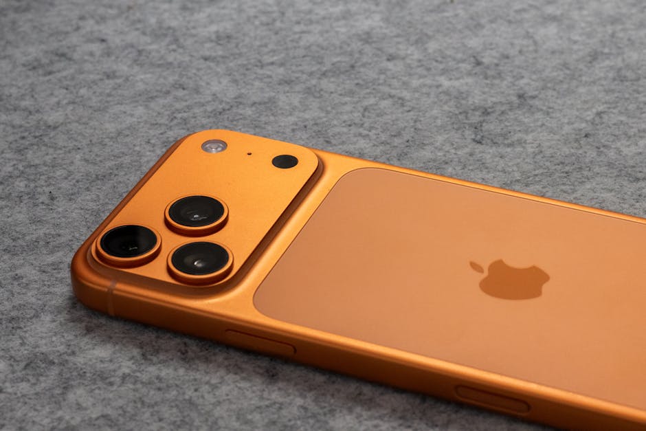 柔らかいグレーの布地の表面にデュアルカメラを搭載したオレンジ色のスマートフォンが置かれています。