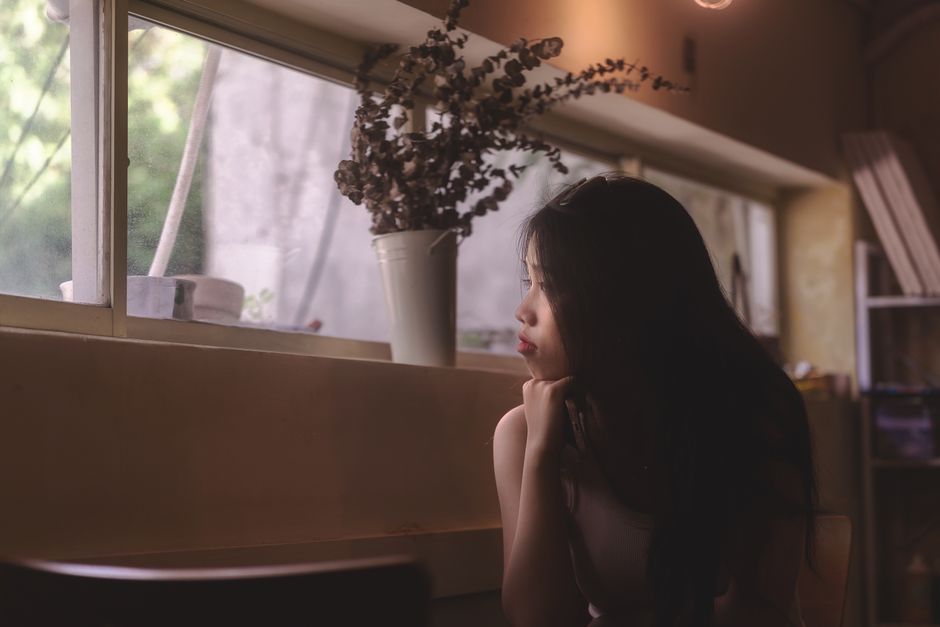 柔らかな室内照明と装飾に囲まれた窓の外を、女性が考えながら見つめています。