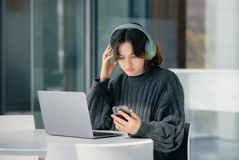 モダンなカフェで、ヘッドフォンをつけてノートパソコンとスマートフォンを使い集中している若い女性。