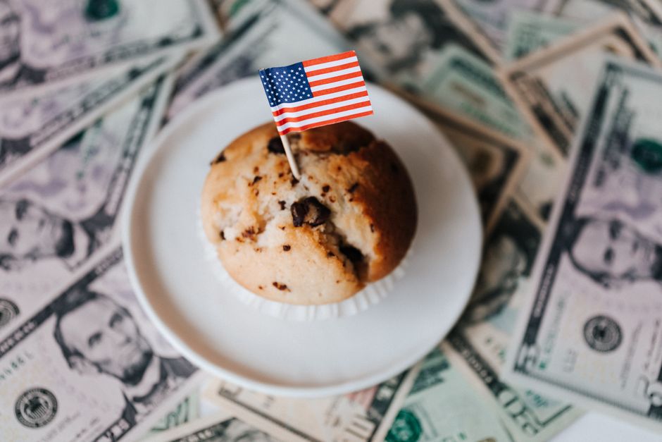 アメリカの旗が乗ったマフィンとドル札に囲まれ、富と愛国心を象徴しています。