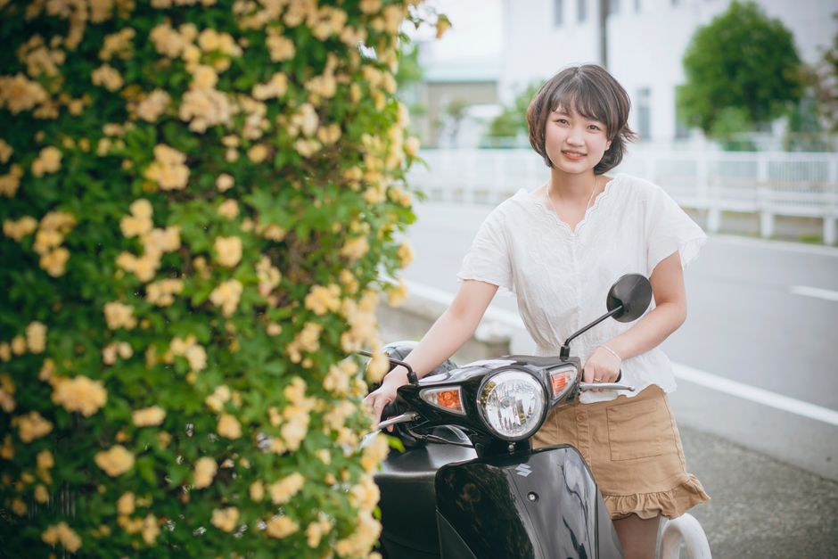 緑に囲まれた街中でスクーターを持って立つ陽気な若い女性。