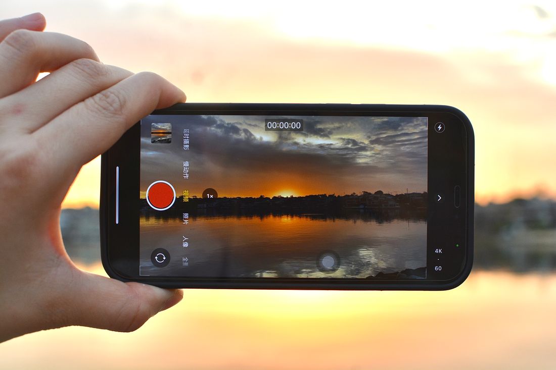 湖畔の鮮やかな夕日と色彩を映し出す写真をスマートフォンで撮影する人物。