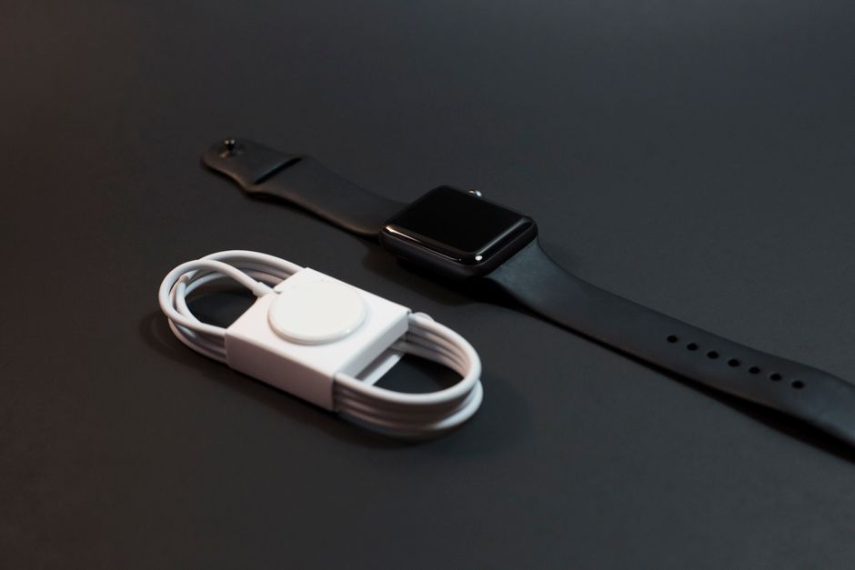 暗い表面に置かれた黒いスマートウォッチと白い充電ケーブルのクローズアップ。技術テーマに最適です。