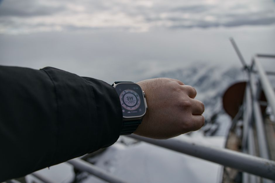 スマートウォッチのコンパスを見ながら雪山を歩くハイカー(Apple Watch Ultra 4の長時間アウトドア利用イメージ)