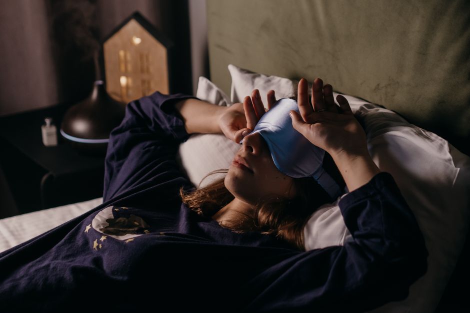 快適な服装をした女性が室内で睡眠マスクを着用して休んでおり、居心地の良い穏やかな雰囲気を醸し出しています。